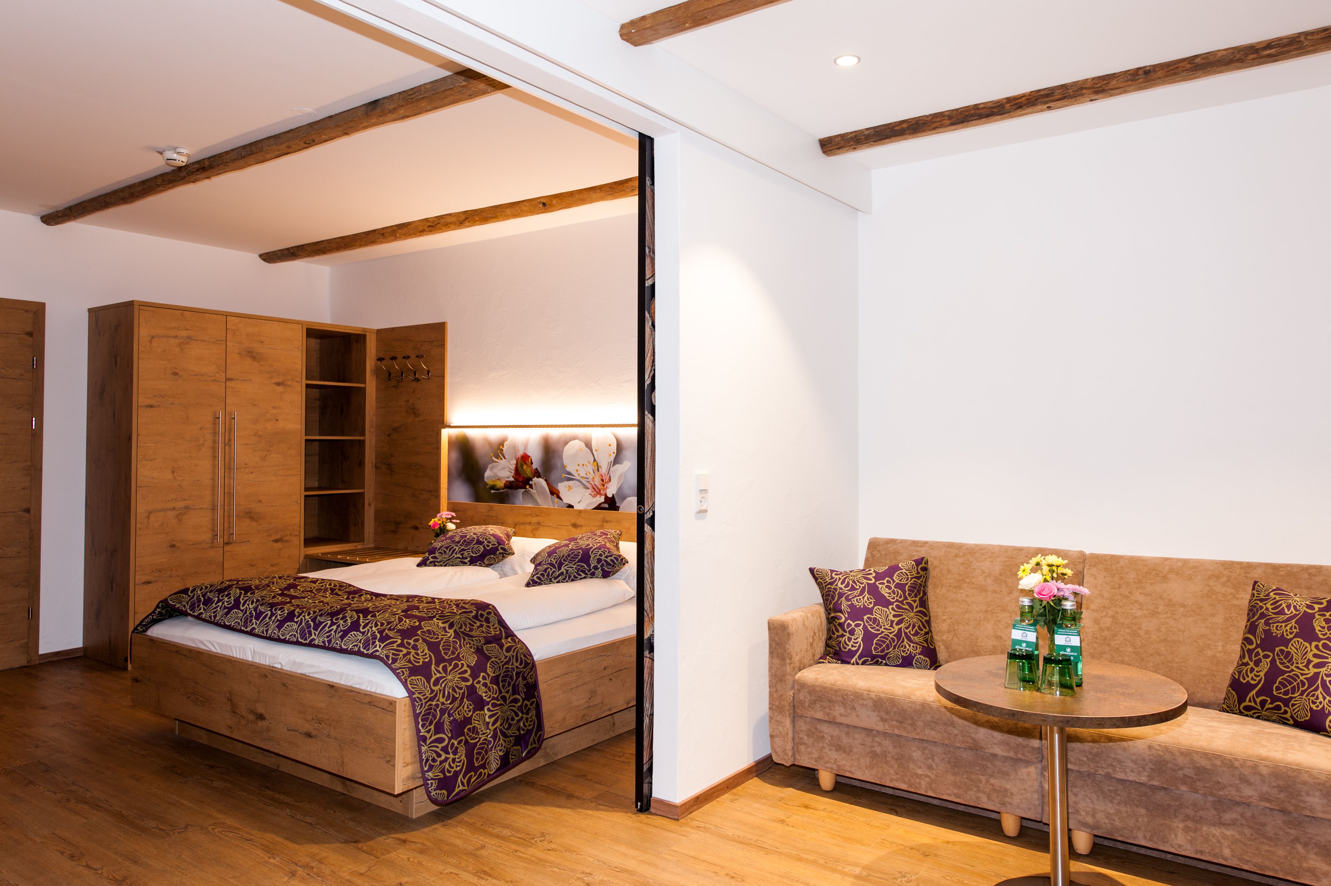 Comfortable hotel room with wooden furniture, double bed, sofa and small table.