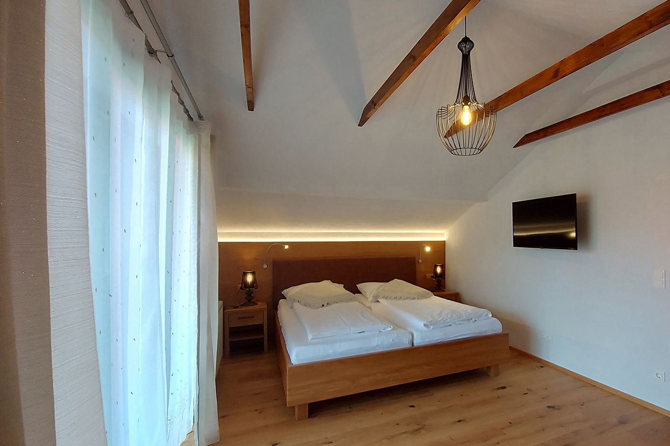 Double room with wooden beams, double bed, bedside tables, lamp and TV on the wall.