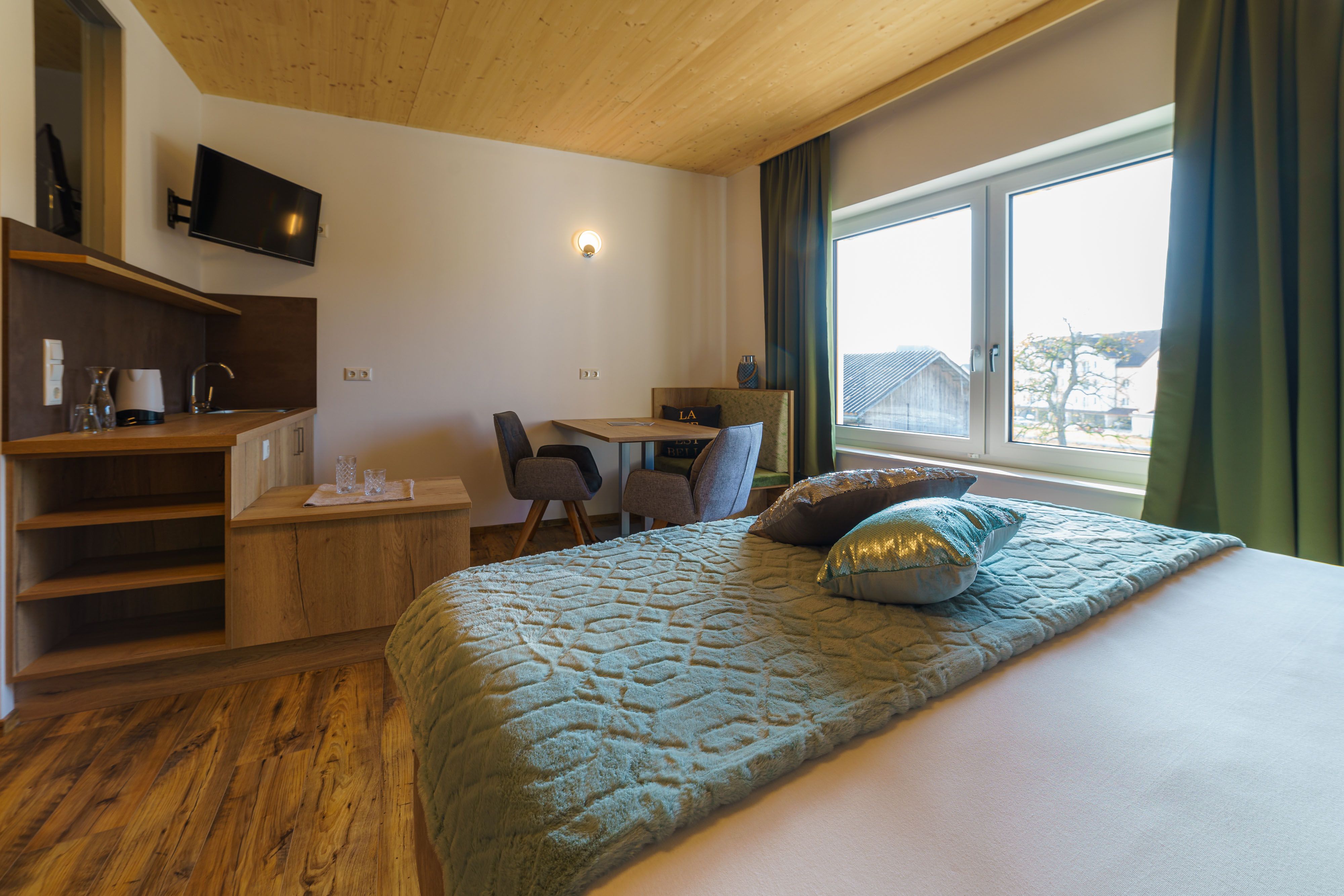Comfortable hotel room with wooden floor, double bed, small table and chairs, TV and large window with a view.
