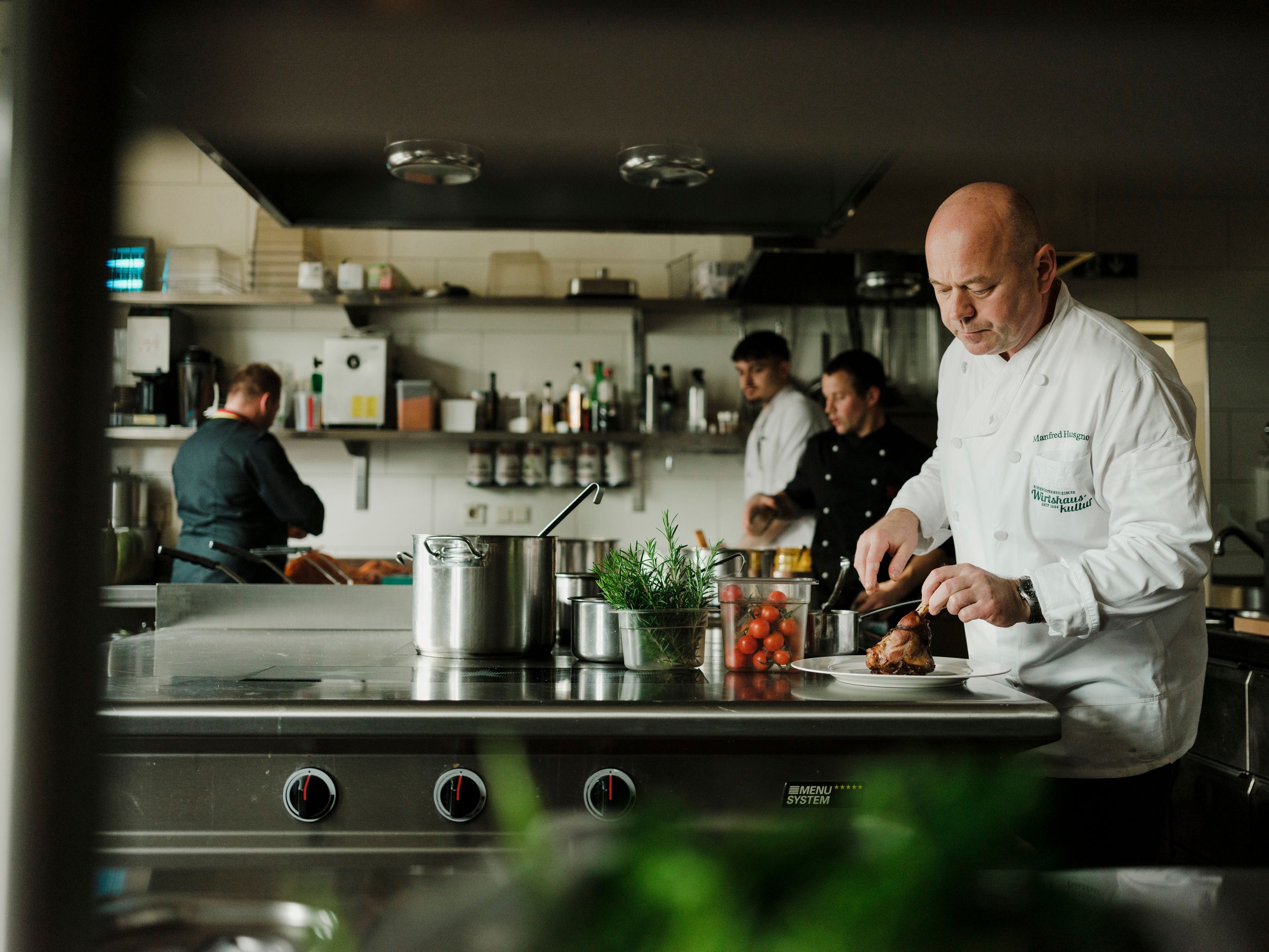 Cooks work in a professional kitchen, one cuts meat.