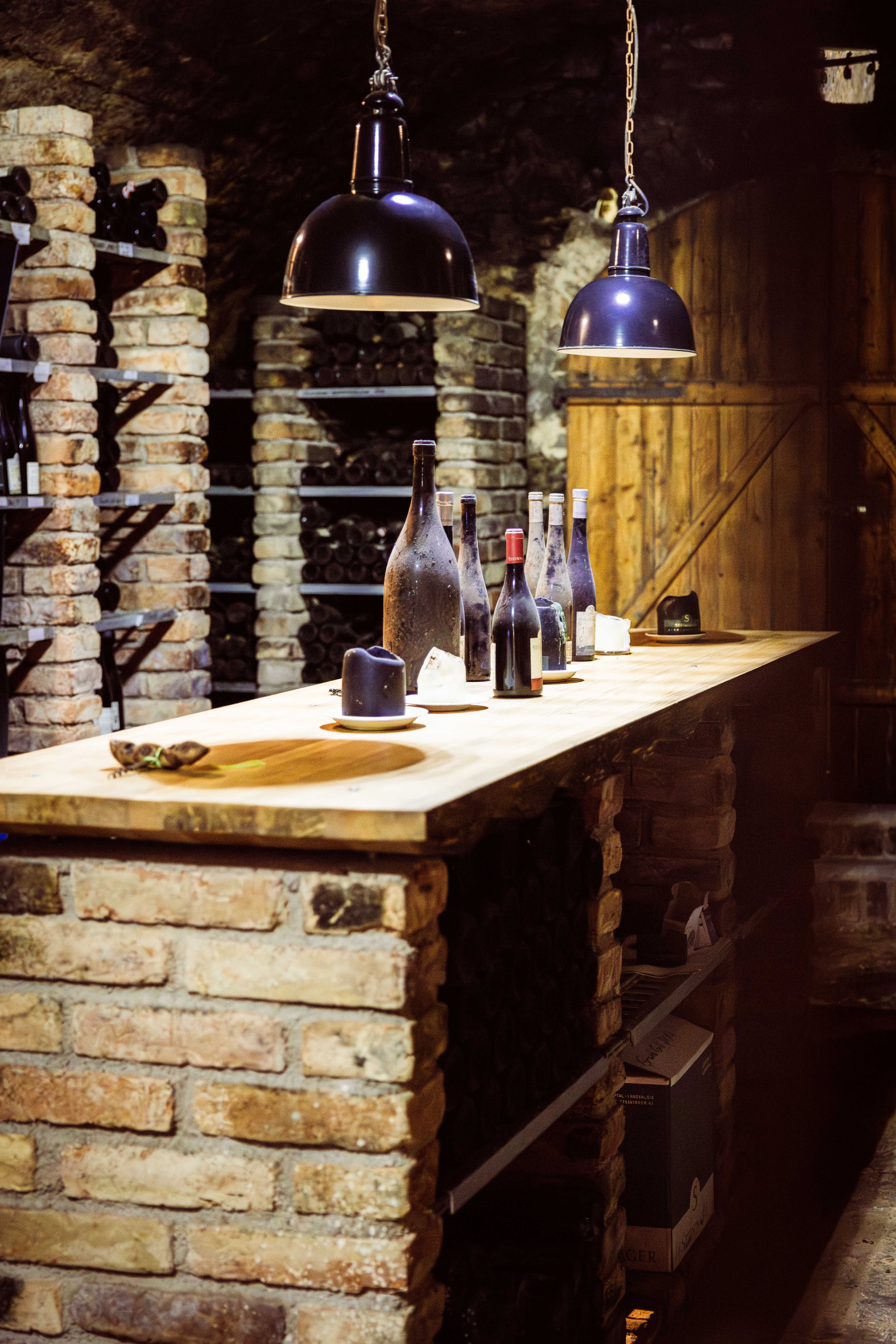 A wine cellar with brick walls, shelves full of wine bottles and a wooden table with several bottles of wine on it.