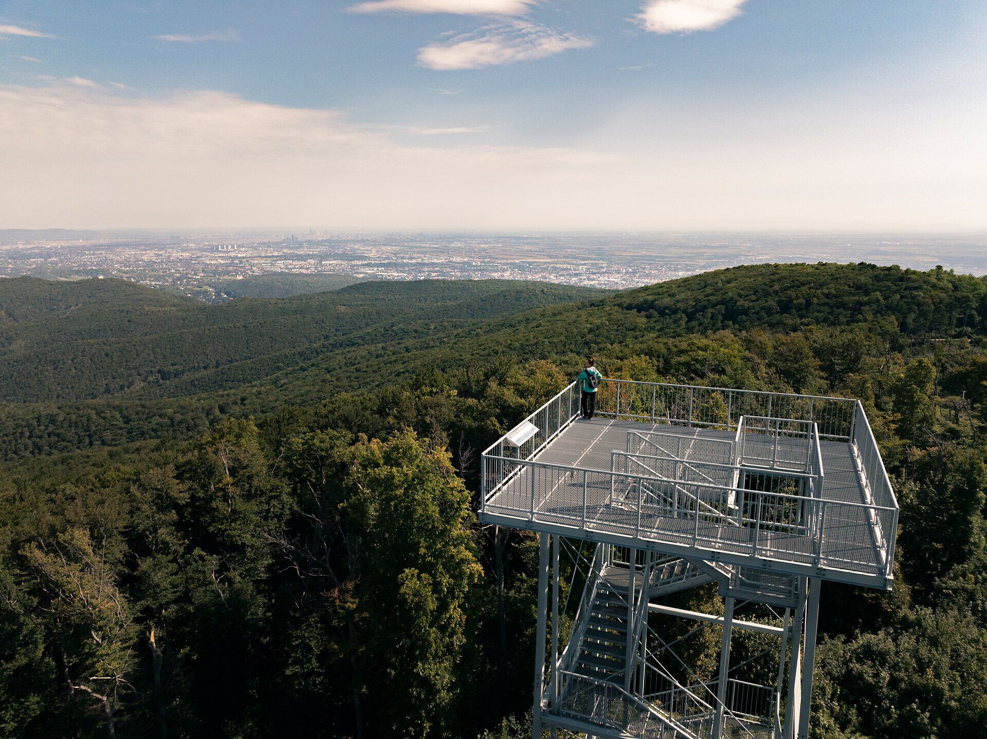 Frau steht oben auf der Jubiläumswarte, umgeben von Wald und urbaner Gegend im Hintergrund
