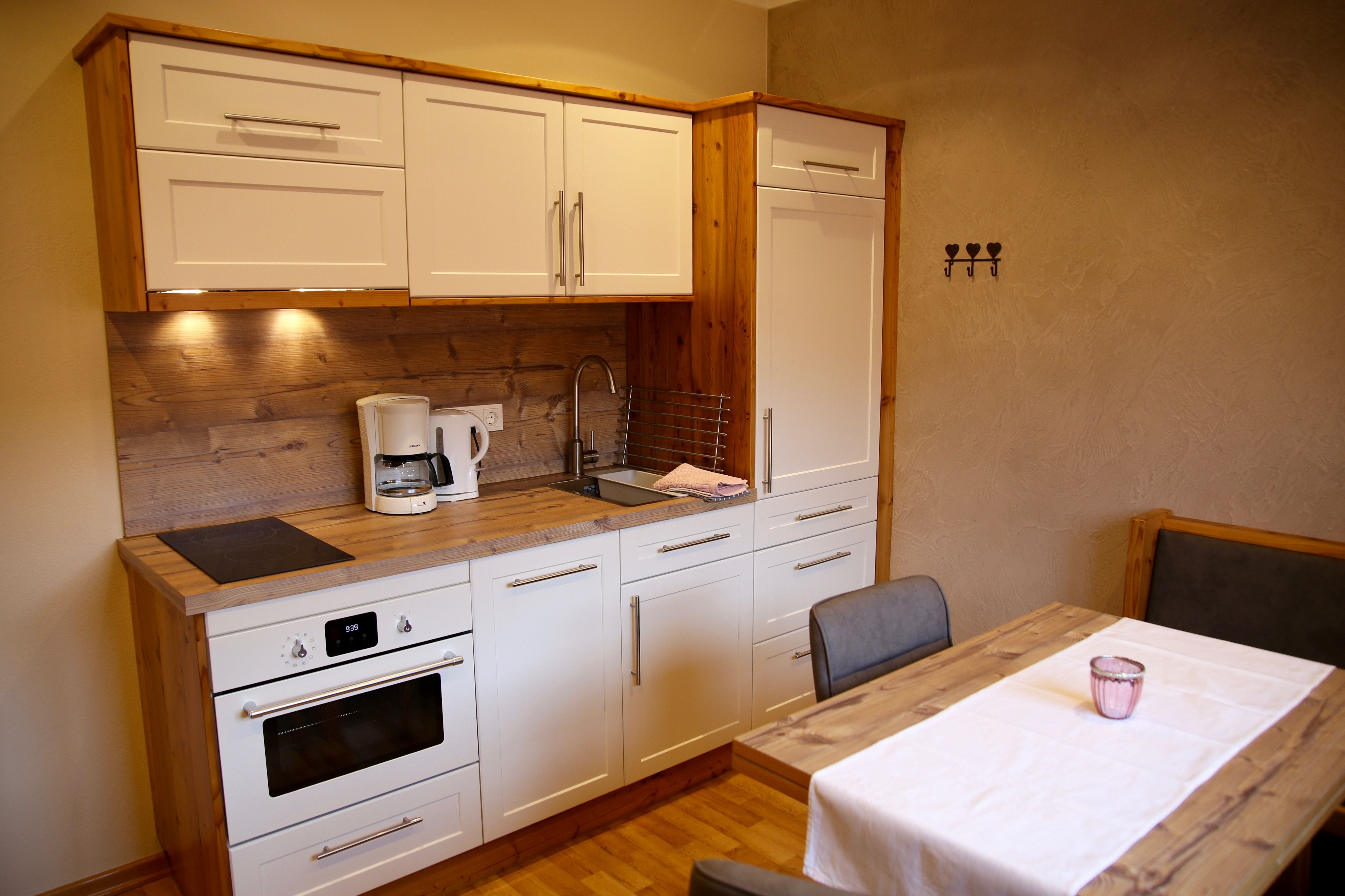 Modern kitchen with white cupboards, wooden worktop, dining table and chairs.