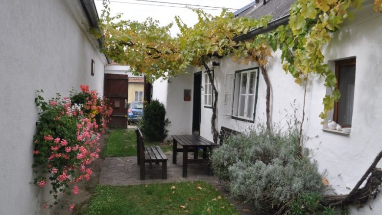 Inner courtyard, © Familie Ackerl A cozy courtyard with a wooden table and benches, surrounded by white walls, flowers and vines.