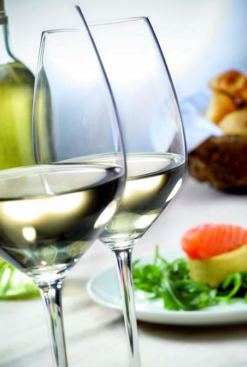 Two wine glasses filled with white wine, in the background a plate with salmon and salad.