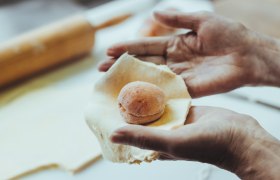 Hands form a dough around an apricot.