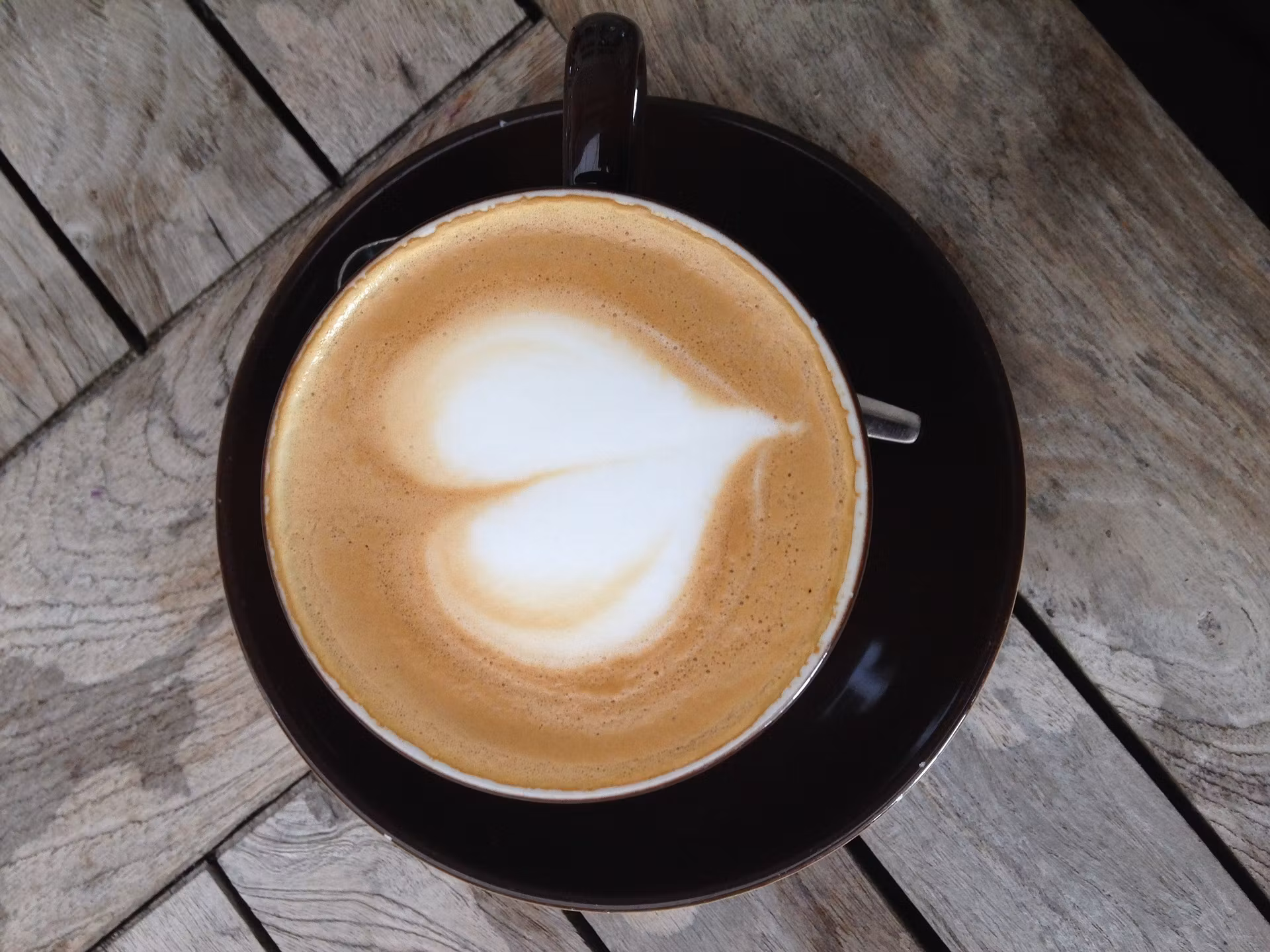 A cup of cappuccino with heart latte art on a wooden table.