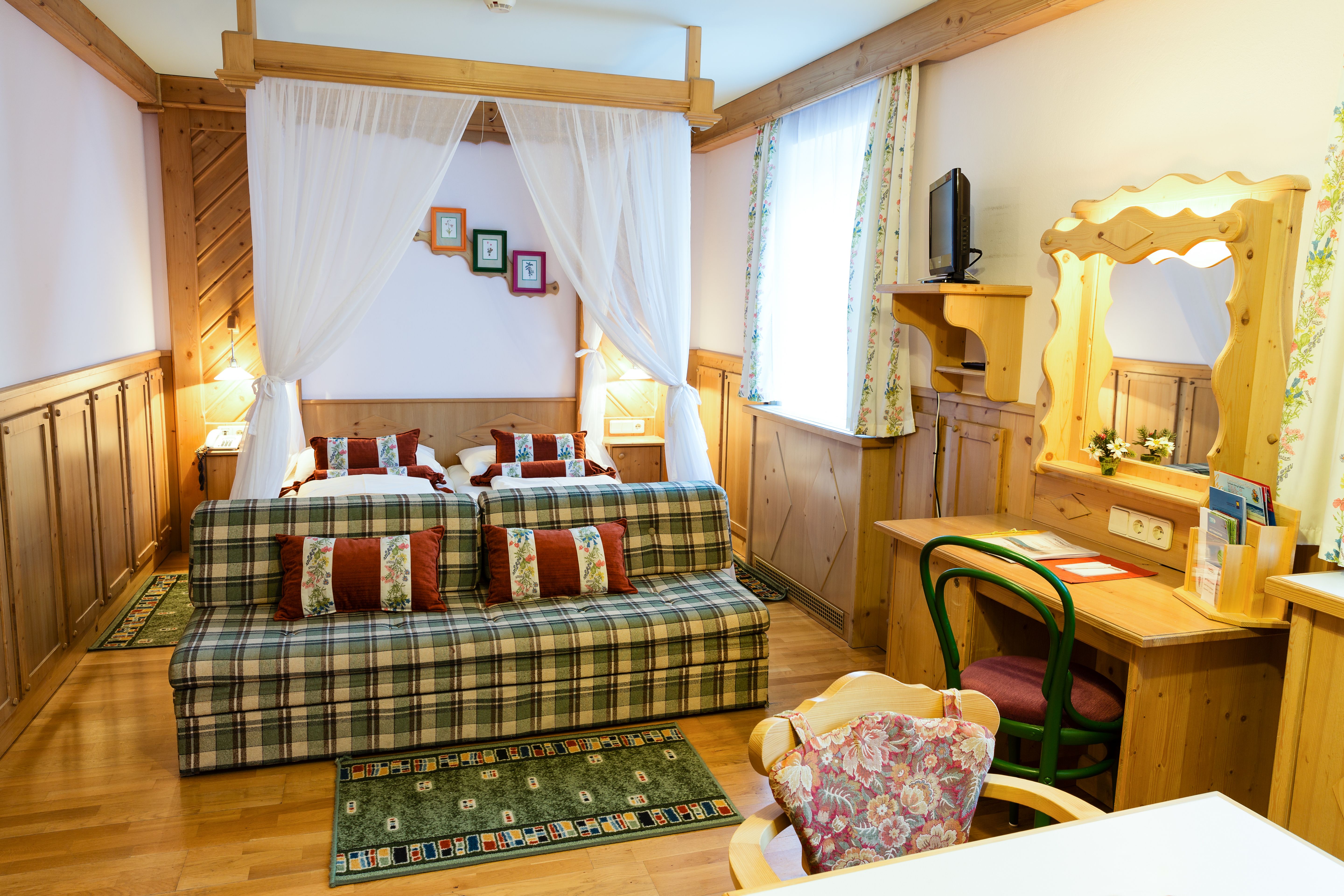 Cozy hotel room with double bed, sofa, desk and mirror in rustic style.