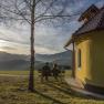 Two people sit on a bench next to a small chapel with a view of the mountains at sunset.
