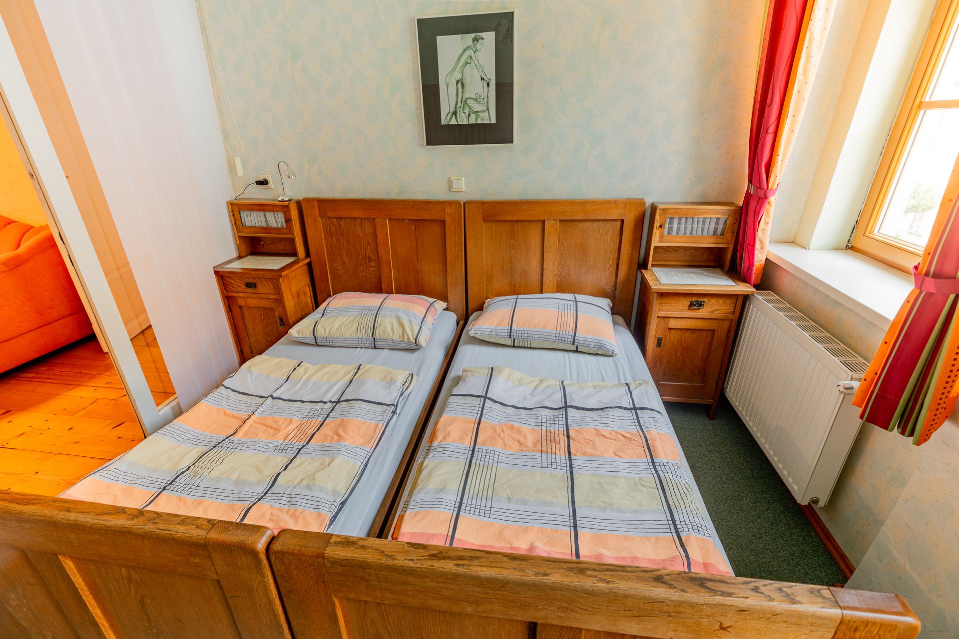 A bedroom with two single beds, wooden furniture and a window with red curtains.