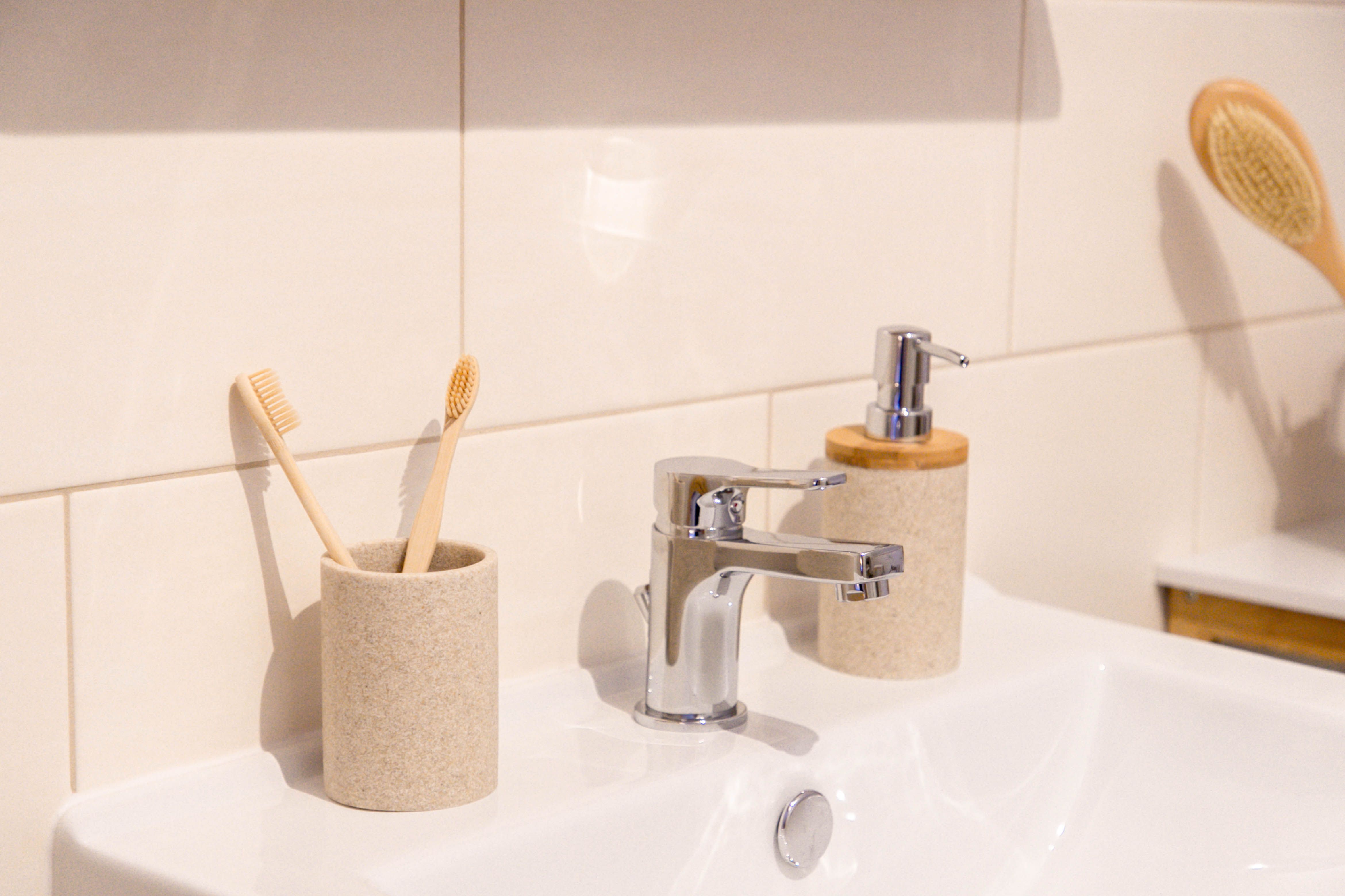 Close-up of a washbasin with two toothbrushes in a cup, a soap dispenser and a brush in the background.
