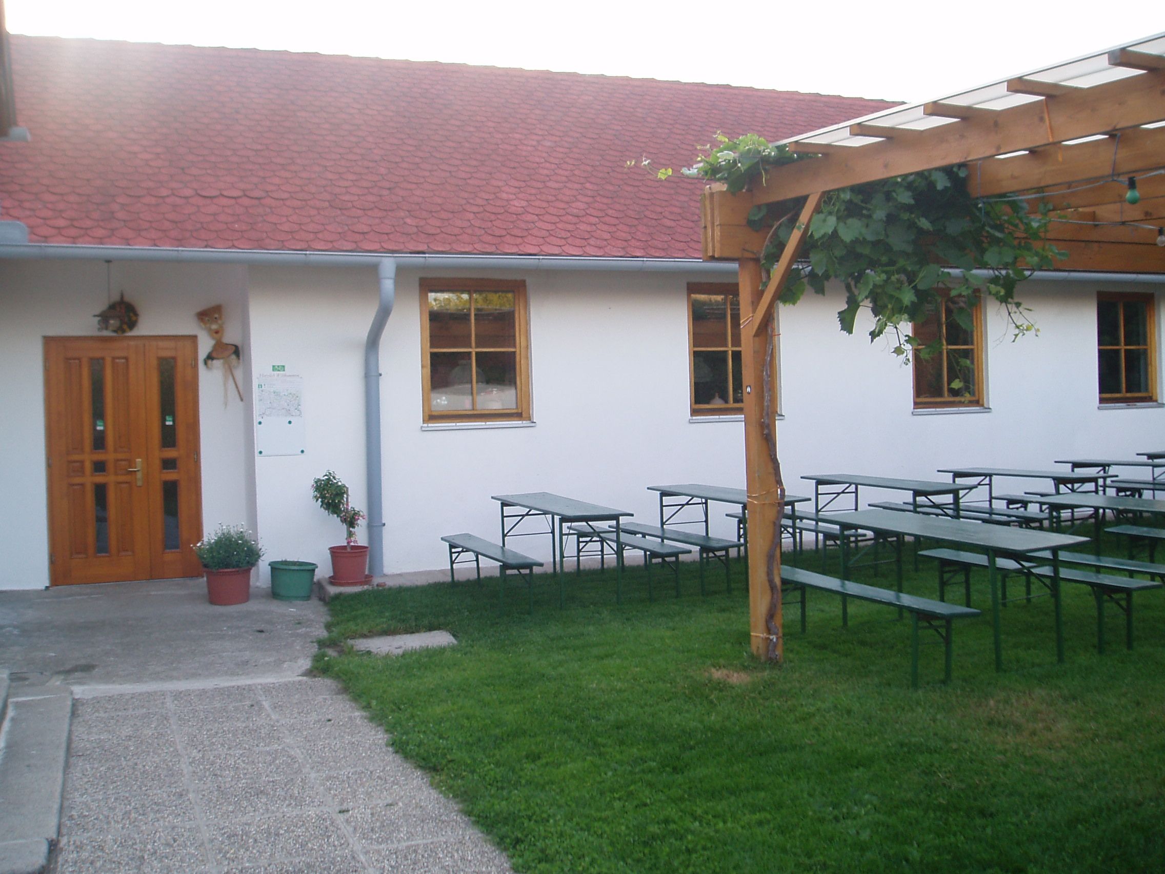 A garden with beer tables, a wooden pergola and a building with red roof tiles.