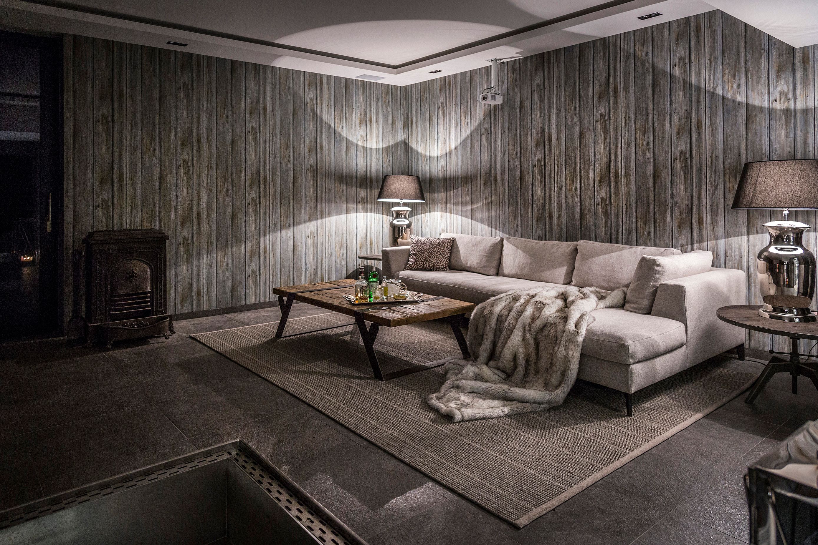 Cozy room with grey sofa, wooden table, fireplace and wood paneling.