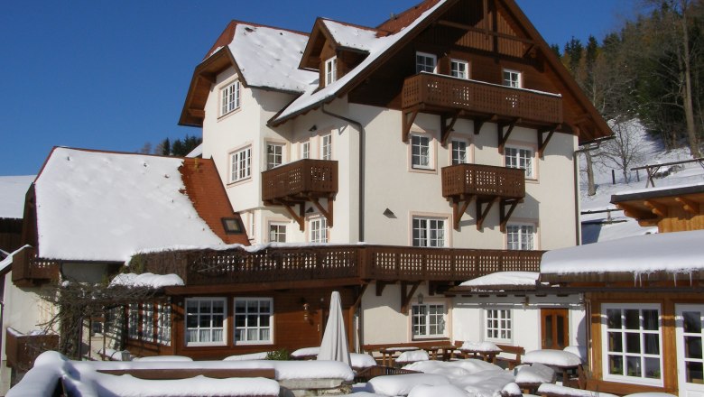 A large, traditional house in the snow with wooden decorations and blue sky in the background.