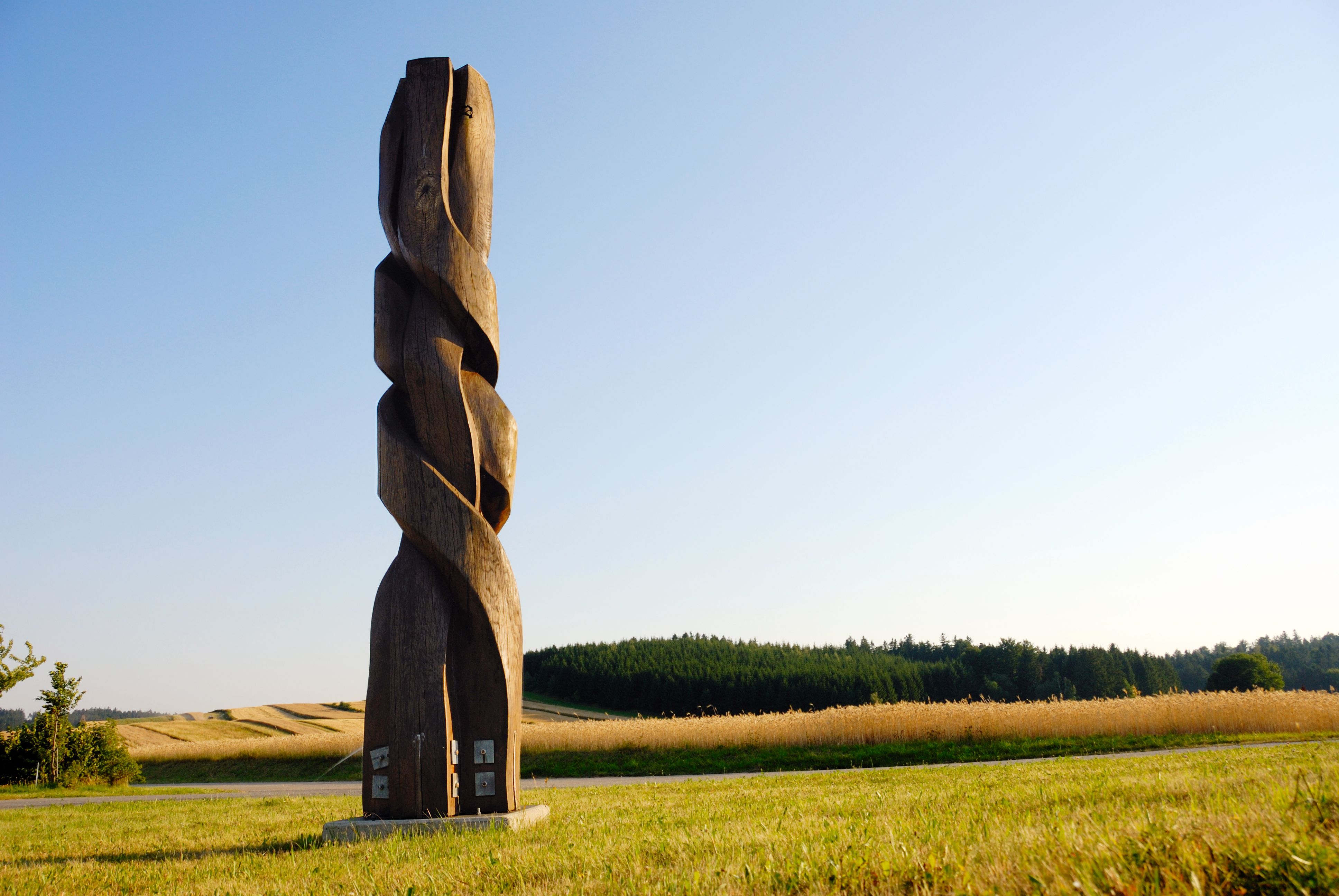 Wooden sculpture in a field with a blue sky in the background.