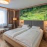 Modern hotel room with double bed, nature picture on the wall, armchair, table and floor lamp.