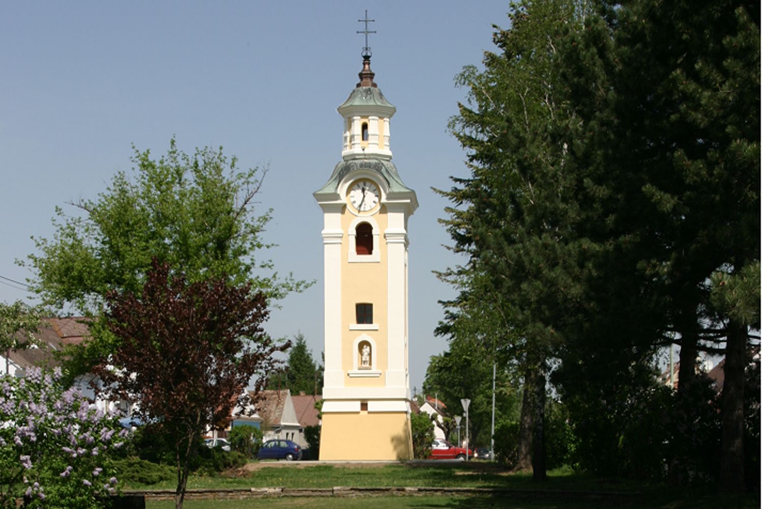 Yellow church tower with clock in Hohenau, surrounded by trees.