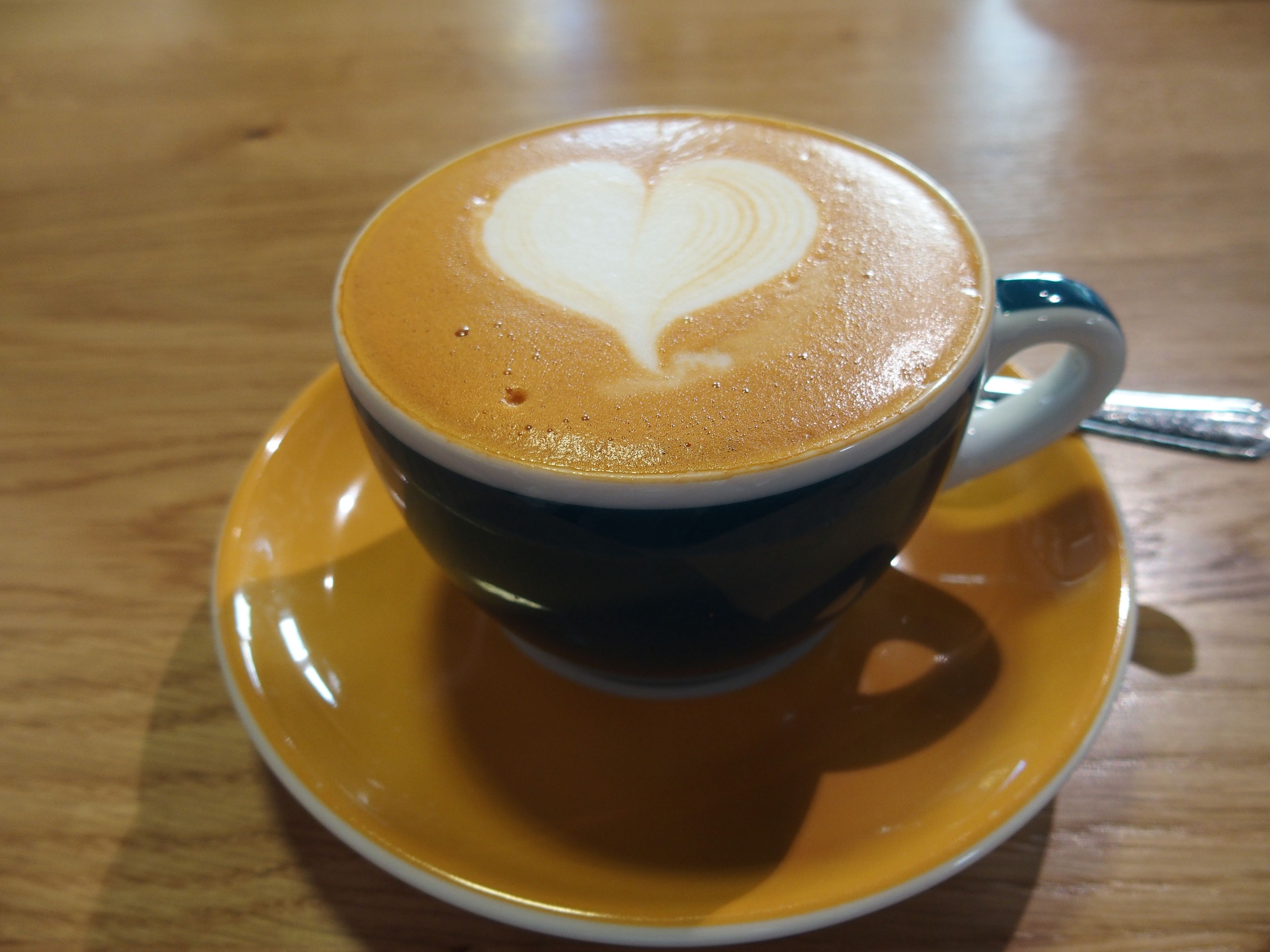 A cup of cappuccino with heart latte art on a wooden table.