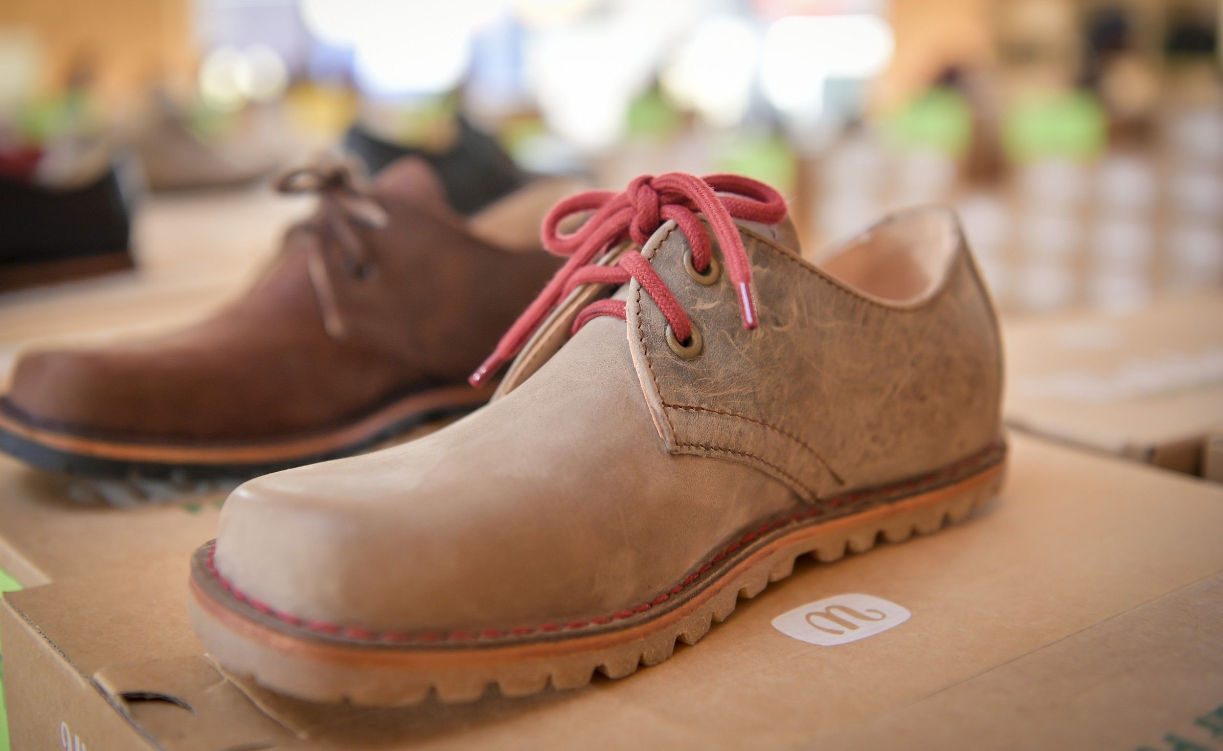 Close-up of a brown leather shoe with red laces on a cardboard box.