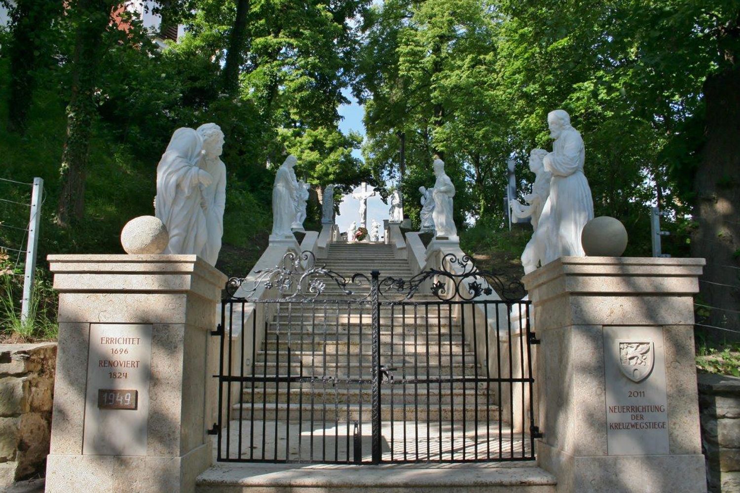 Stone staircase with white statues and a wrought-iron gate.