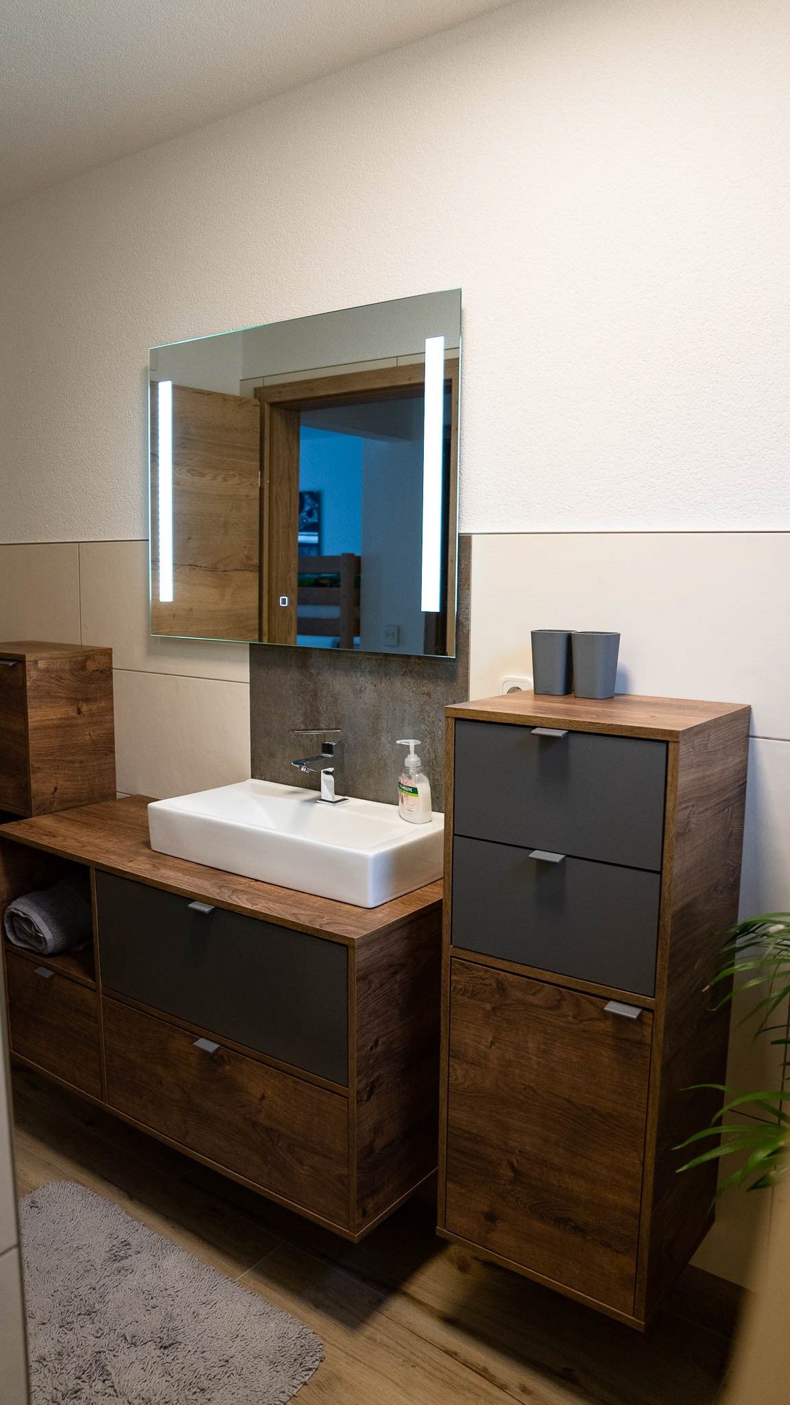 Modern bathroom with wooden cabinets, washbasin and illuminated mirror.