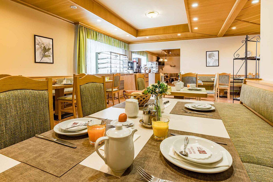 A cozy breakfast room with laid tables, juice glasses and coffee pots.