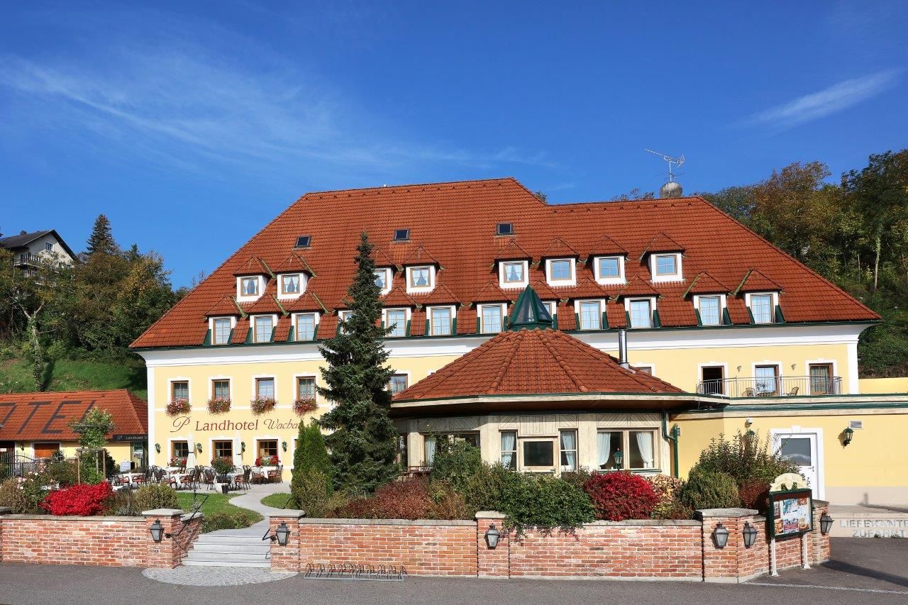 Exterior view of a yellow country hotel with a red roof and garden.