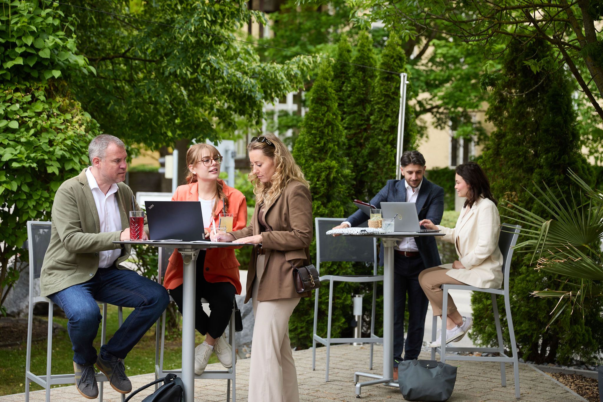 People working outdoors at high tables with laptops.