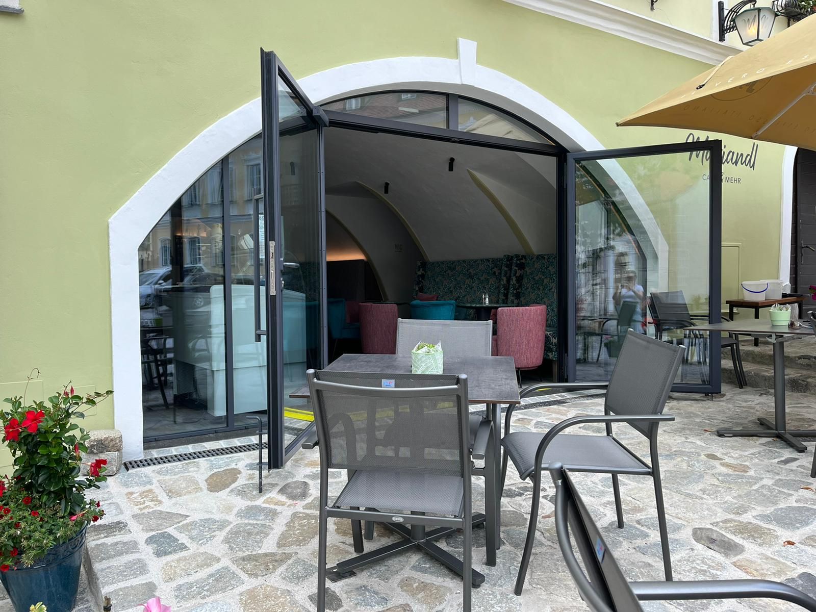 Exterior view of a café with open glass doors and outdoor seating.