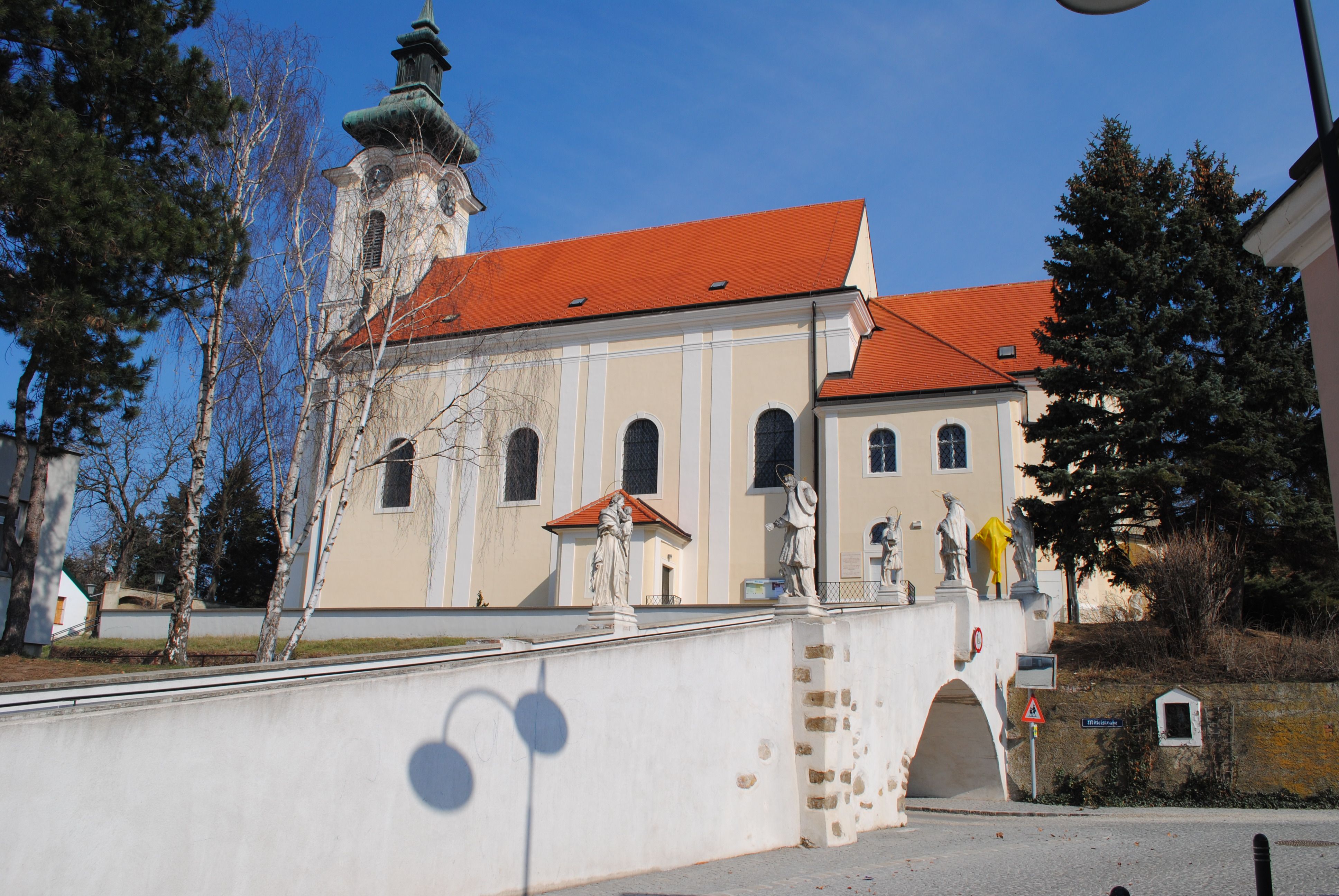 Wolkersdorf parish church with statues on a bridge, blue sky.