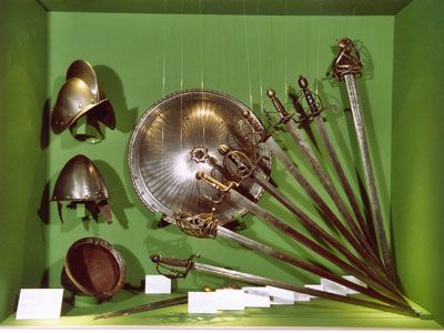 Exhibition of antique weapons and helmets in a green display case.