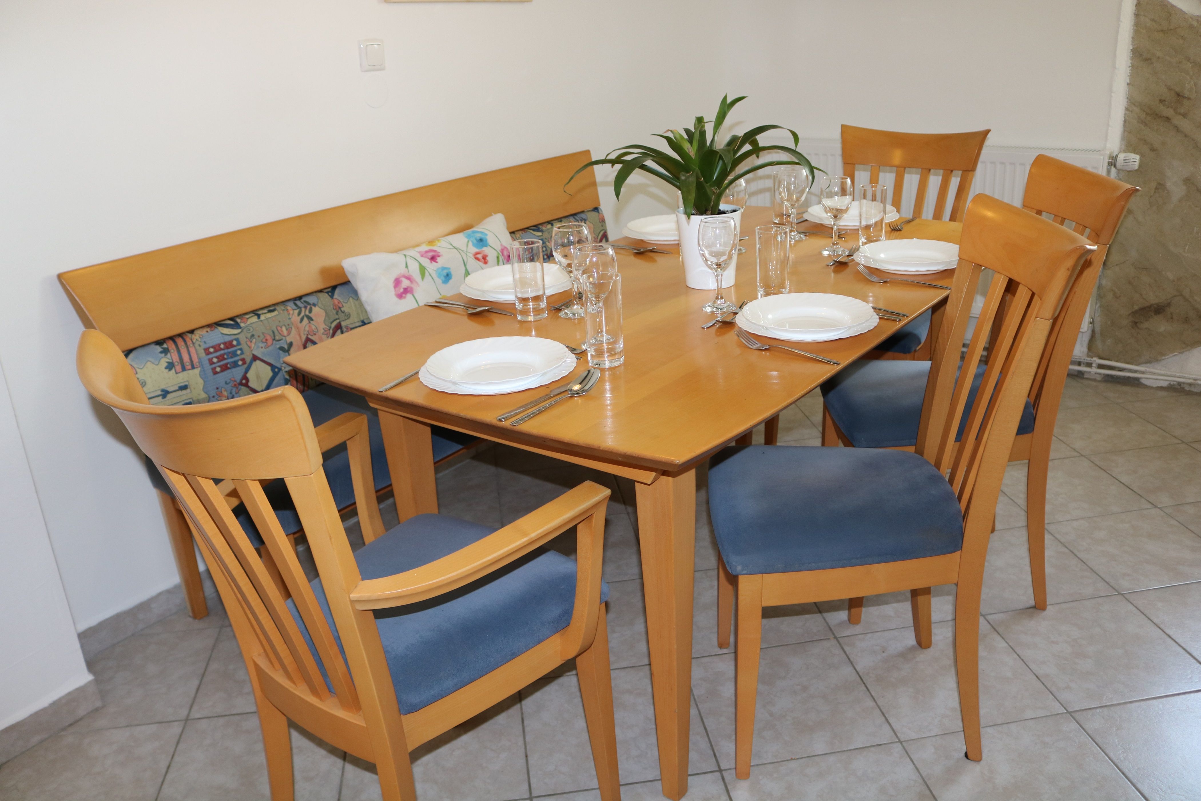 Dining area with wooden table, six covered seats and blue chairs.