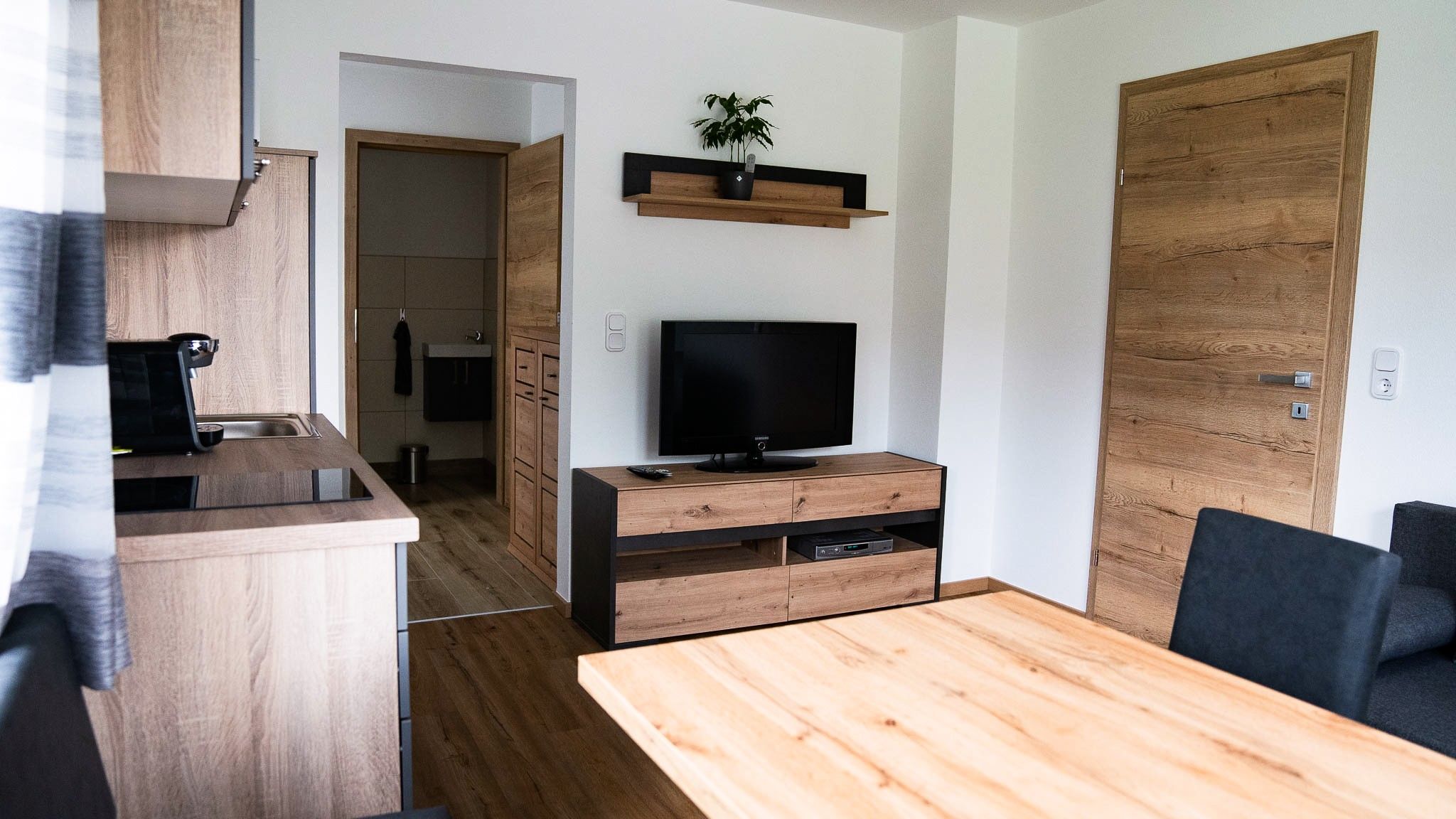 Modern living room with wooden furniture, TV and kitchen.
