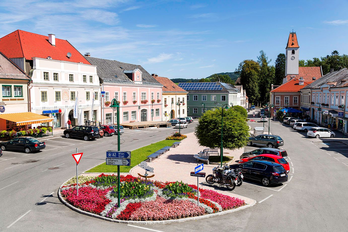 Main square in Aspang Markt with colorful flowerbeds, parked cars and historic buildings.