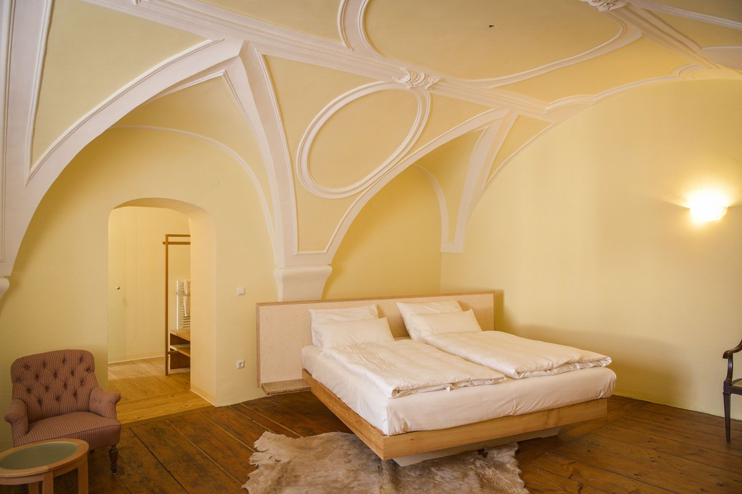 An elegant bedroom with a vaulted ceiling, a double bed, an armchair and wooden floor.