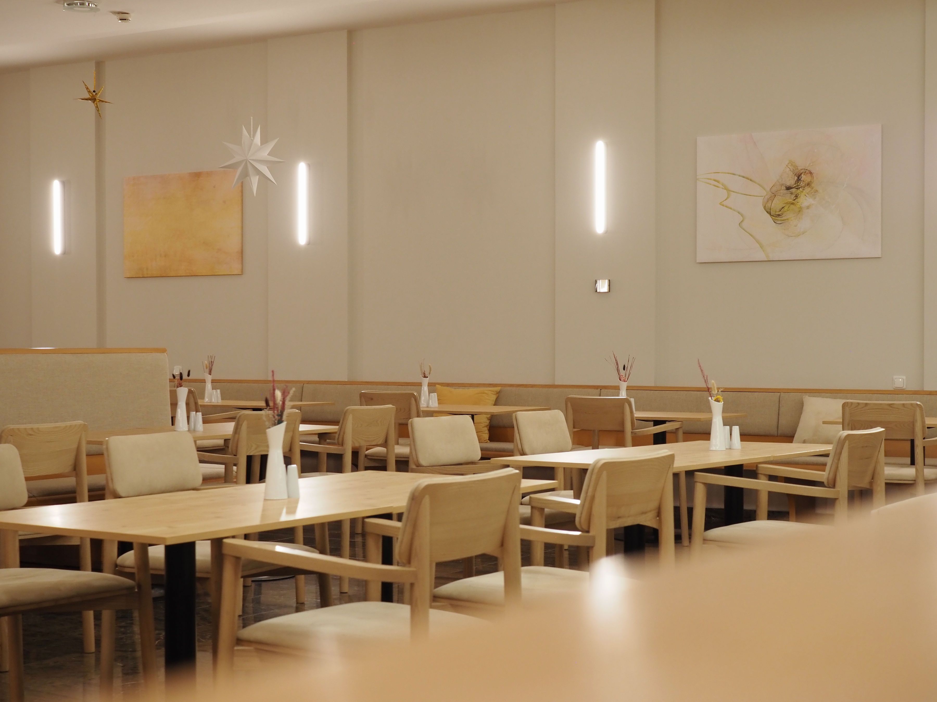 Interior view of a modern restaurant with wooden tables and chairs, decorated with minimalist artwork and star pendants.