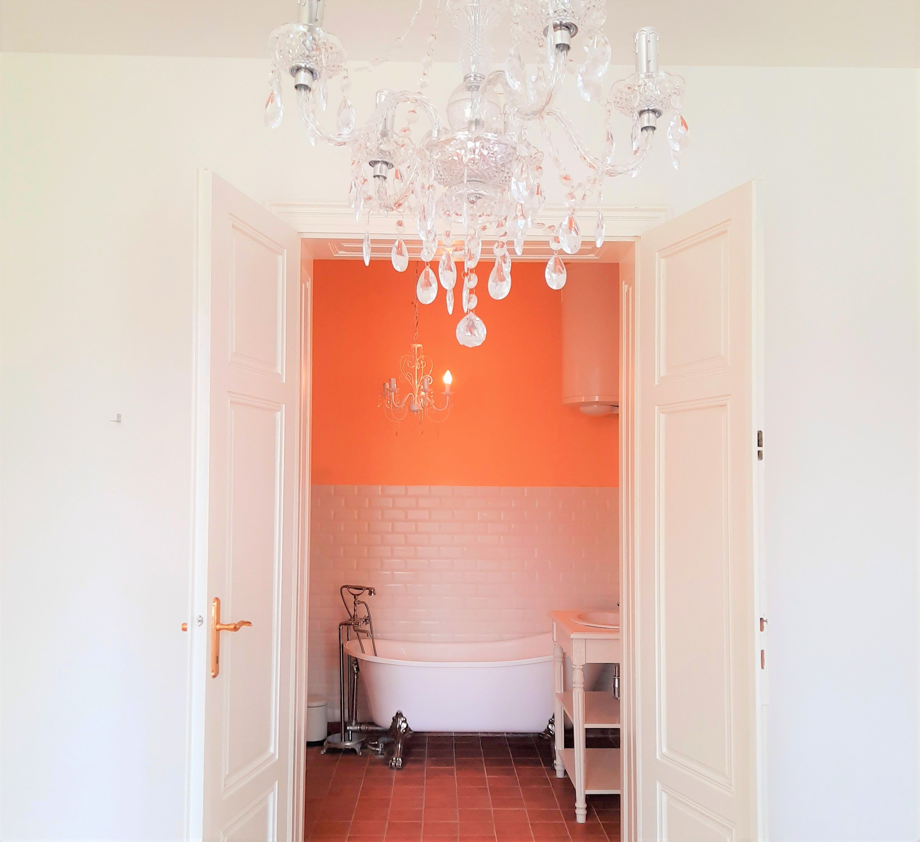 View of a bathroom with free-standing bathtub, orange wall and chandelier.