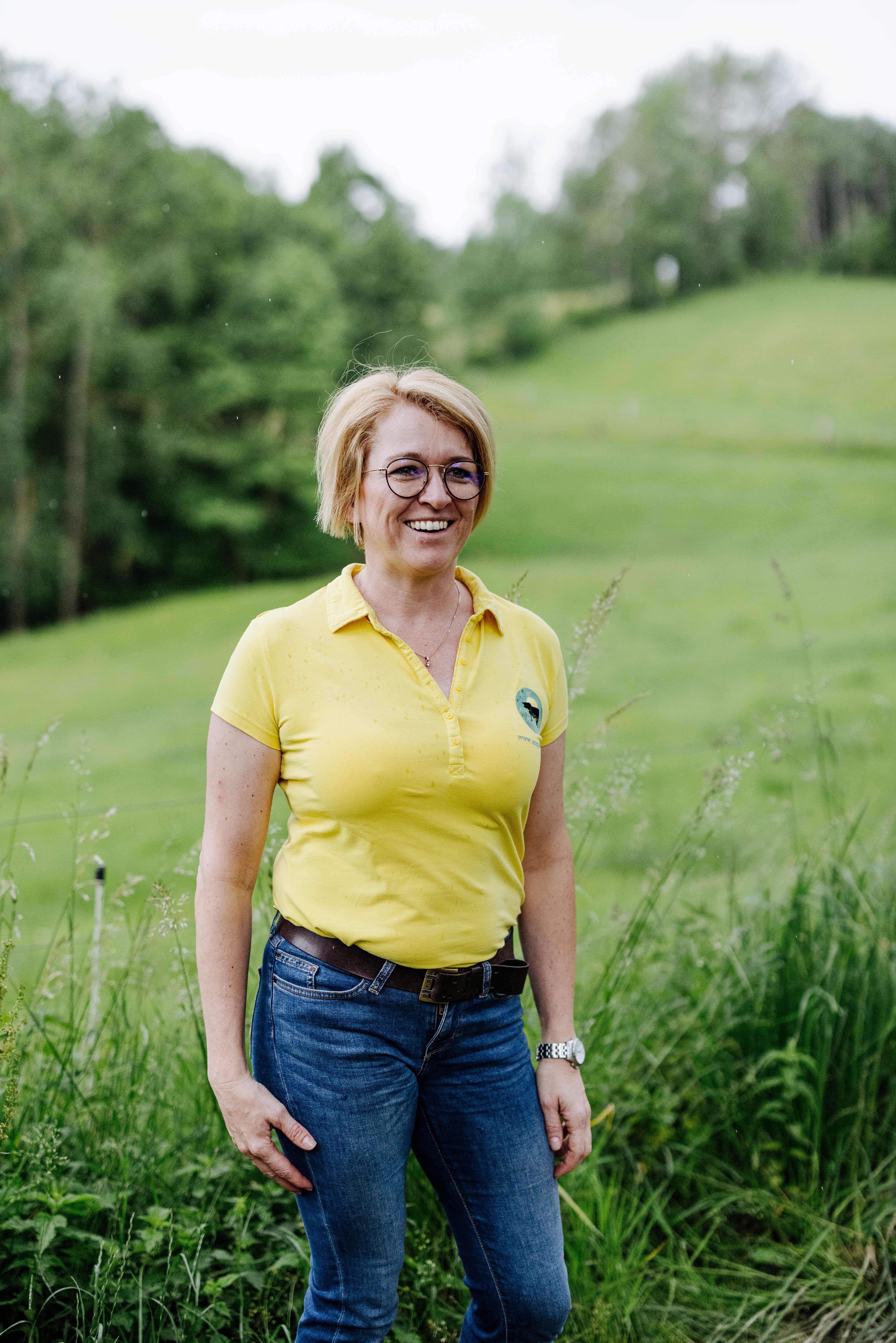 The owner, Sandra Anderl, stands smiling on a green meadow.