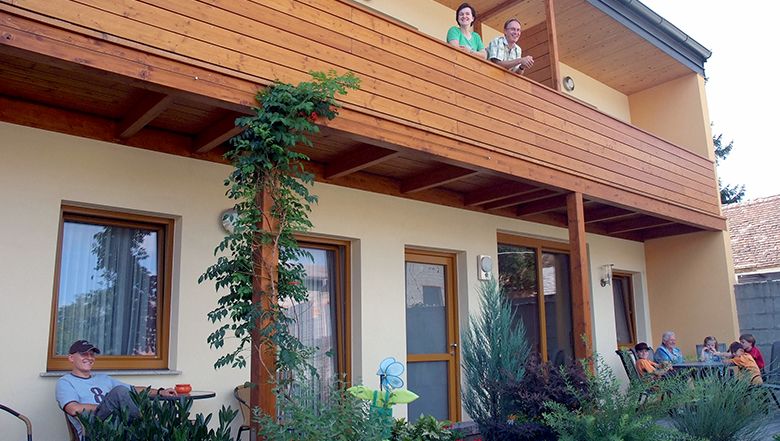 People on a balcony and in the garden of a two-story house.