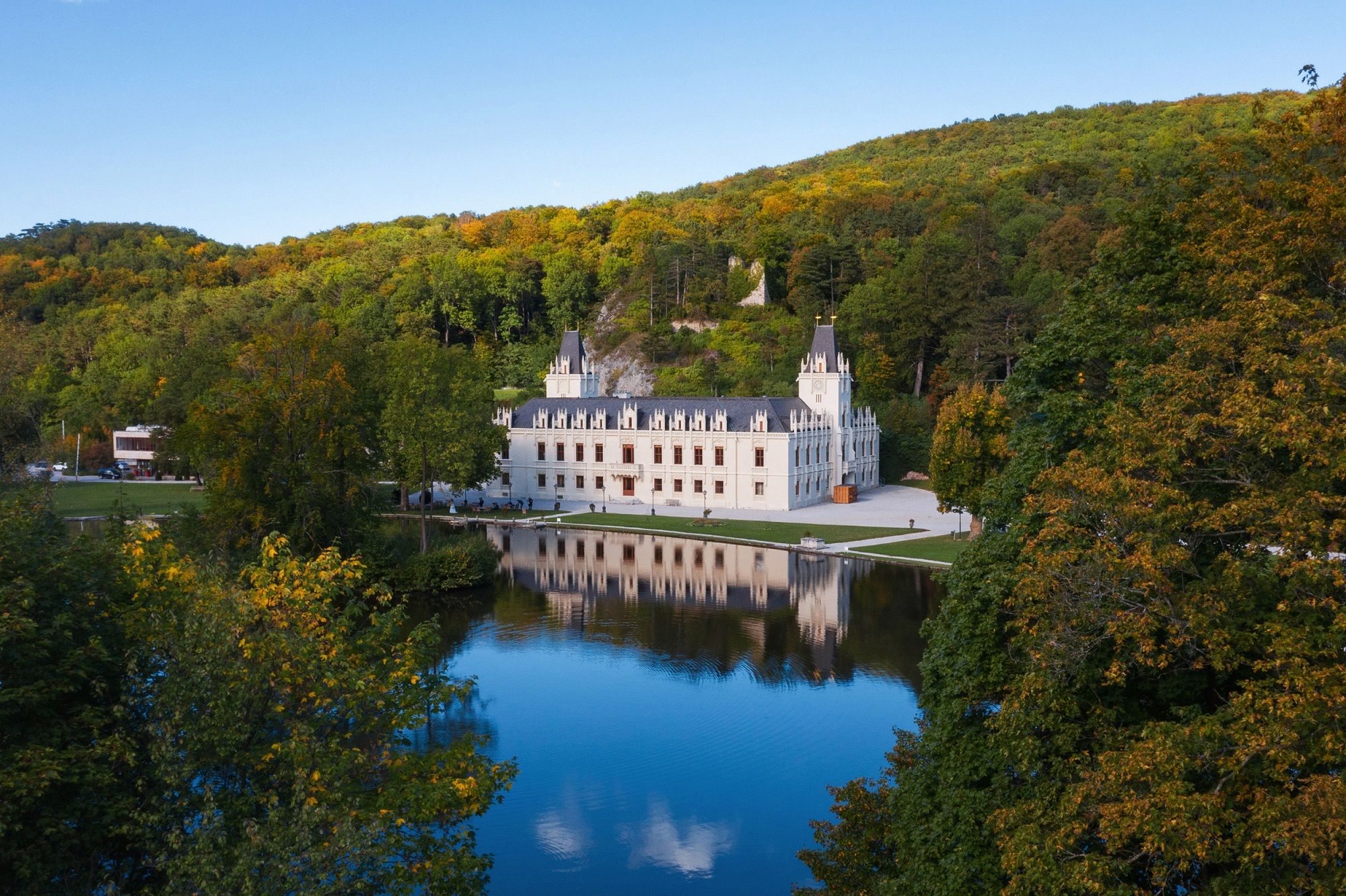 Schloss Hernstein with reflection in the water, surrounded by trees and hills.