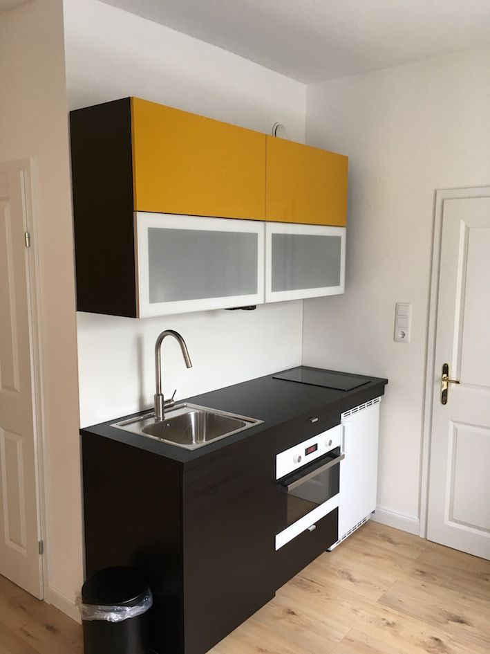Small modern kitchen with yellow wall units, sink, hob and oven.