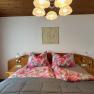 A cozy bedroom with a double bed, floral bedding and a wooden ceiling. A lamp hangs from the ceiling.