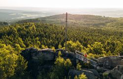 Aussichtsplattform auf einer Felsformation mit Blick über dicht bewaldete Hügel im Waldviertel, unter einem klaren blauen Himmel.
