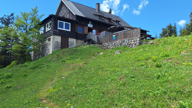 A mountain hut on a green meadow under a blue sky.