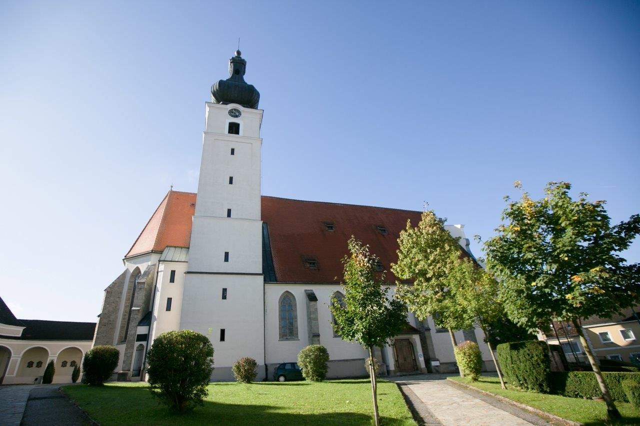 Mank pilgrimage church with tower and red roof, surrounded by trees and lawn.