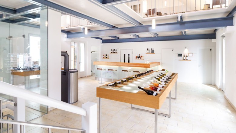 Interior view of a modern wine shop with wine bottles on a table and a bar in the background.