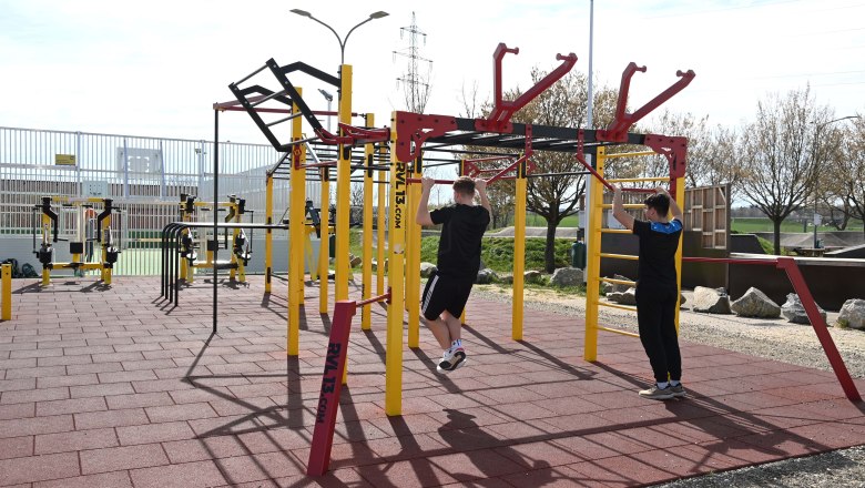 Two people train on a calisthenics scaffold outdoors.