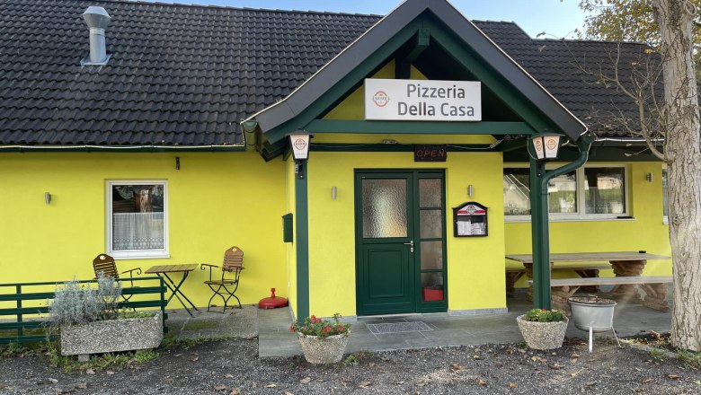 Exterior view of a yellow pizzeria with the name 'Pizzeria Della Casa'.