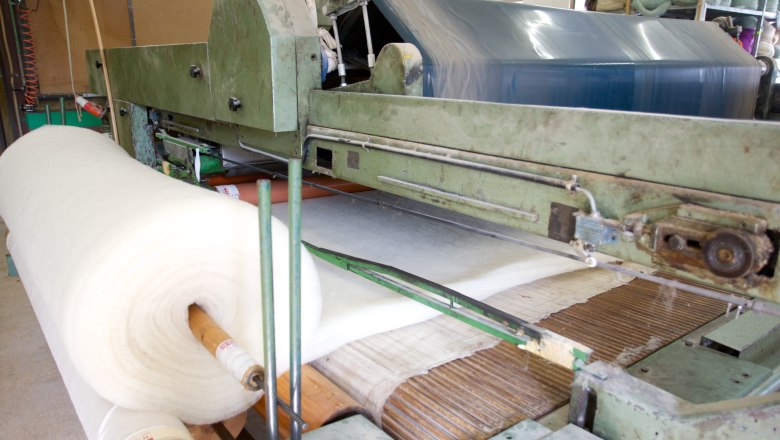 Machine in a wool workshop with large rolls of white wool material.
