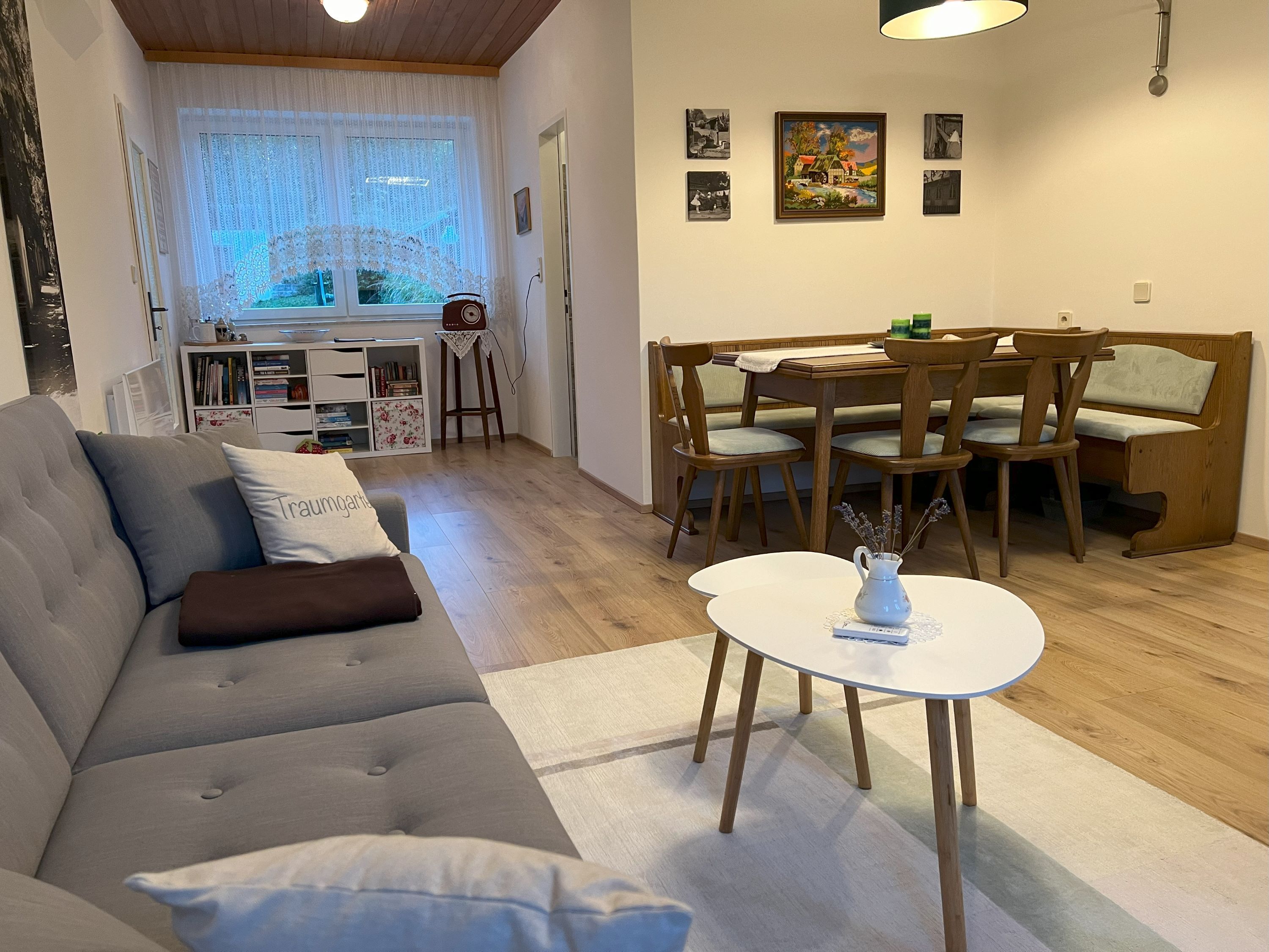 Cozy living room with grey sofa, dining table and chairs, bookshelf and window with curtains.